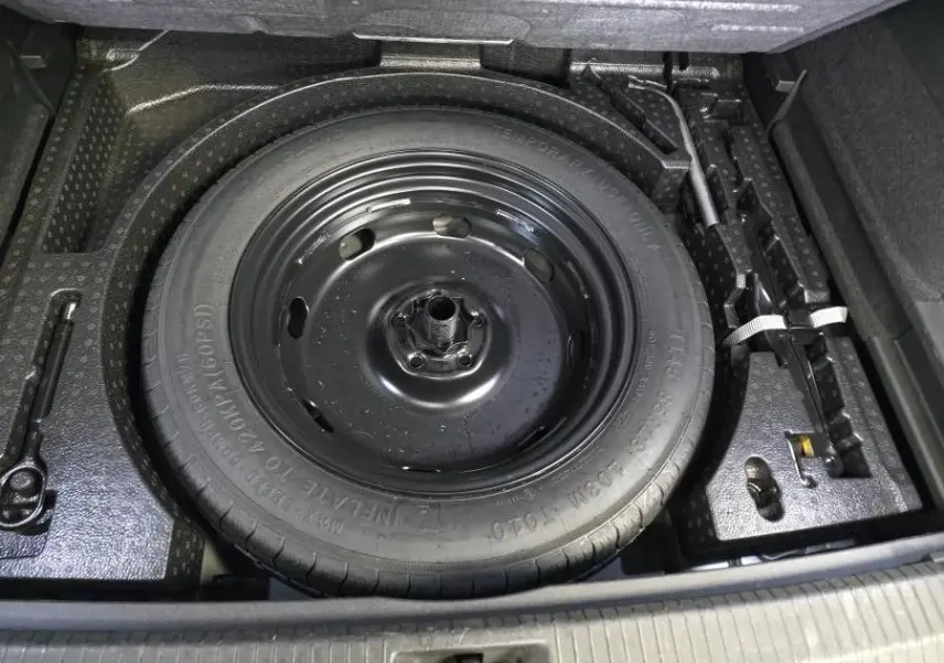 Vue rapprochée de la roue de secours compacte noire dans le coffre du Volkswagen Tiguan 2025 noir.
