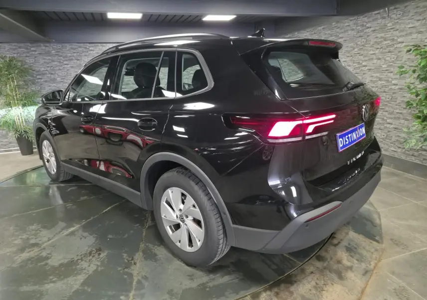 Volkswagen Tiguan noir 3/4 arrière droit en intérieur, feux arrière allumés et jantes alliage 17 pouces.