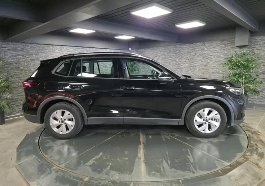 Vue de profil côté gauche d'un Volkswagen Tiguan noir 2025 avec jantes alliage 17 pouces dans un showroom intérieur.