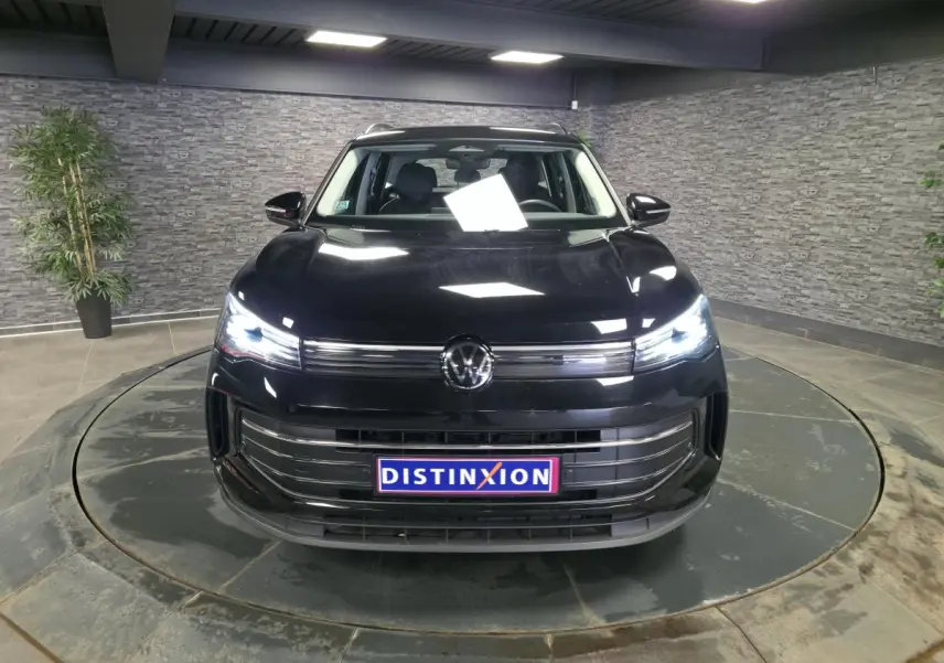 Volkswagen Tiguan noir 2025 vue de face avec phares LED allumés dans un showroom fermé.