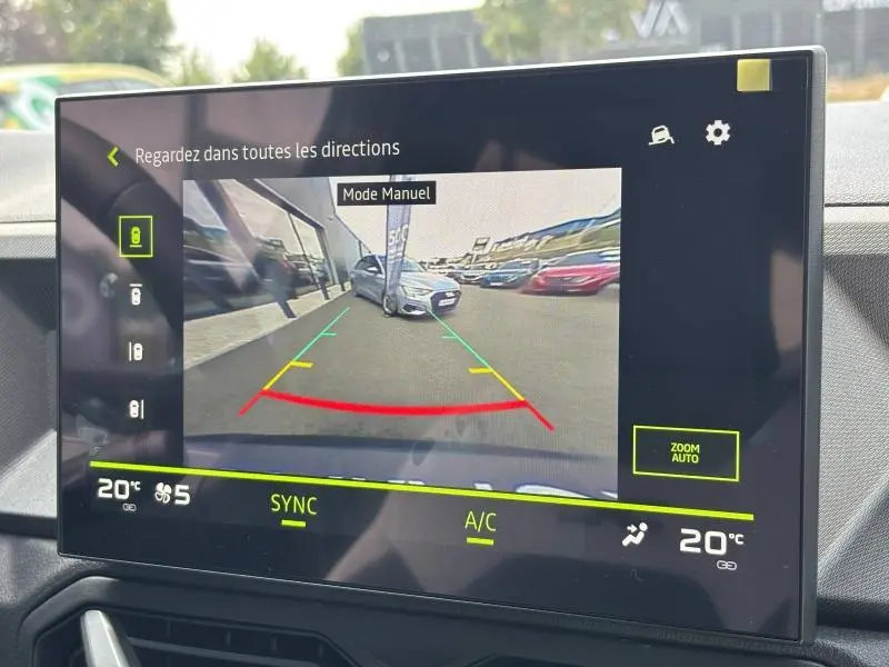 Écran tactile montrant la caméra de recul avec vue arrière sur un véhicule blanc stationné côté droit.