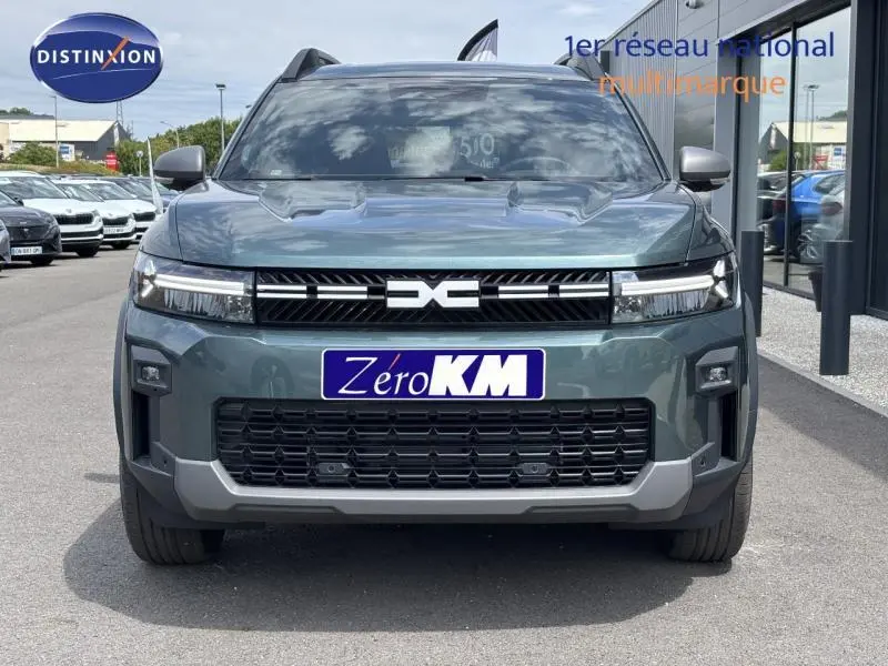 Vue frontale d'un Dacia Bigster gris avec calandre noire et logo central distinctif sur un parking.
