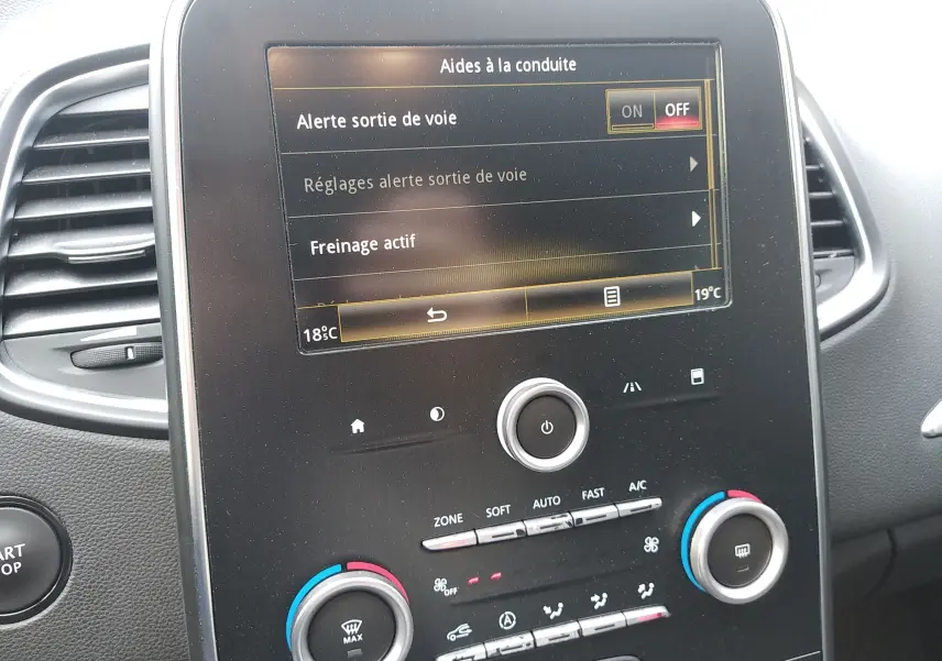 Écran tactile central du tableau de bord du Renault Grand Scenic IV brun, affichant les aides à la conduite et la climatisation.