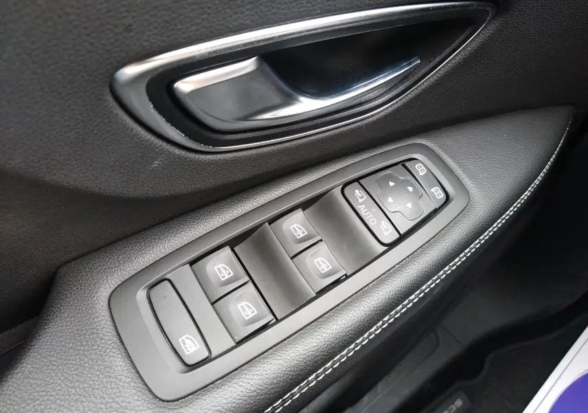 Gros plan sur la commande des vitres et rétroviseurs côté conducteur du Renault Grand Scenic brun avec surpiqûres blanches.