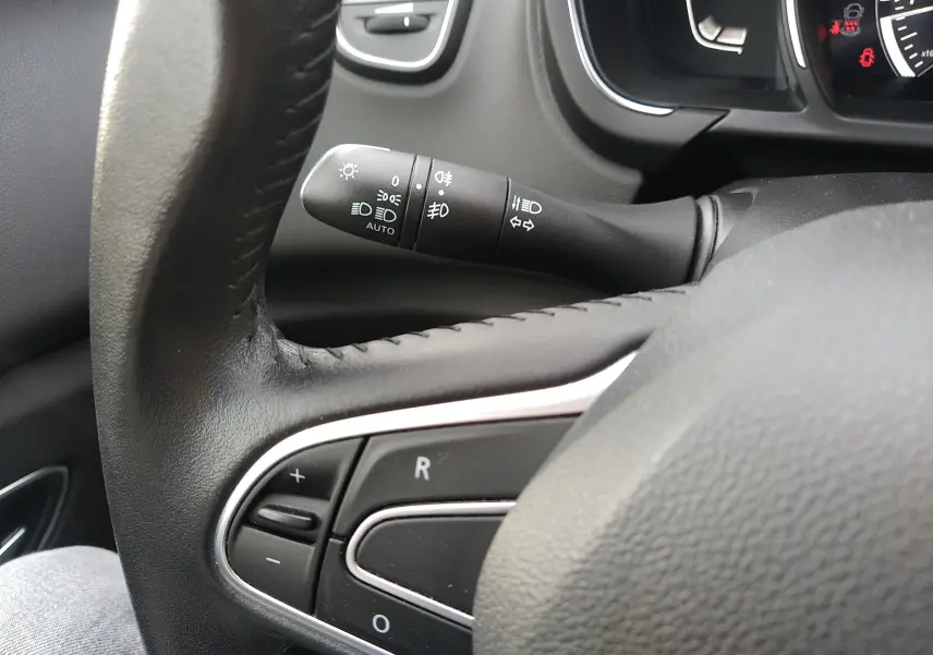 Gros plan sur le commodo des phares et les commandes au volant en cuir noir du Renault Grand Scenic IV.