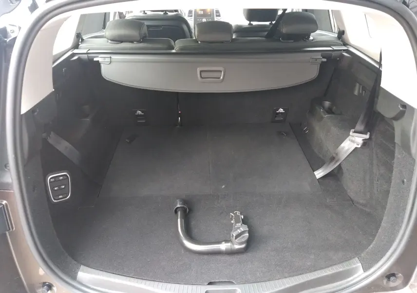 Coffre ouvert d'un Renault Grand Scenic brun vison métal, vue arrière montrant l'intérieur spacieux et la barre d'attelage amovible.