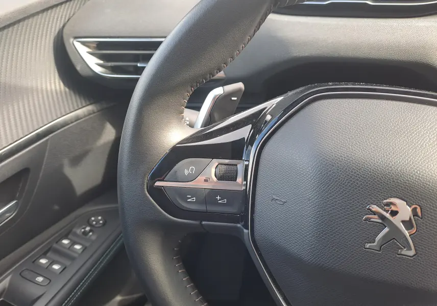 Gros plan sur le volant noir du Peugeot 3008 Hybrid 145 Allure Pack 2024, avec commandes intégrées et logo lion chromé.