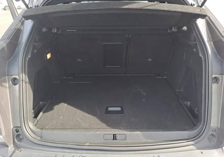 Coffre ouvert d'un Peugeot 3008 Hybrid gris platinium, vue arrière montrant l'espace de chargement vide et la moquette noire.