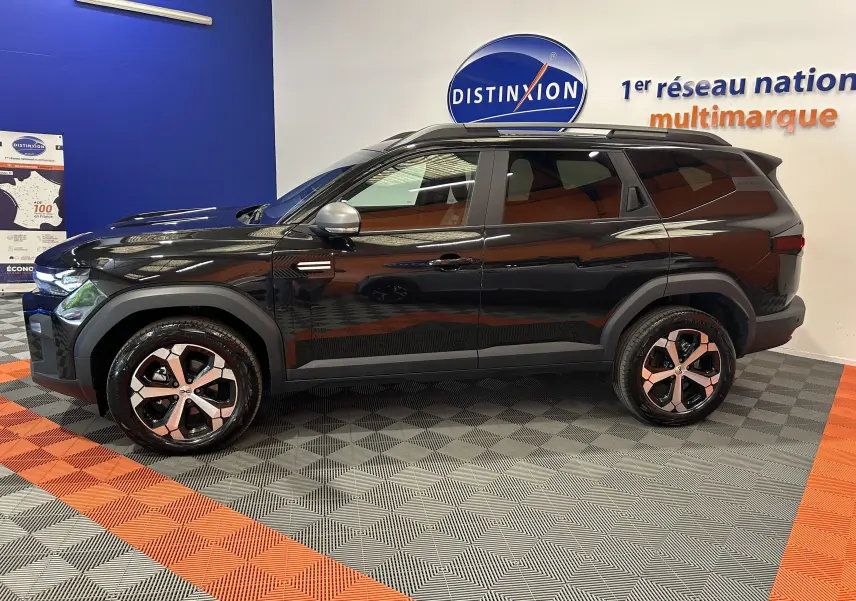 Vue latérale droite du SUV Dacia Bigster noir nacré avec jantes bicolores et toit ouvrant en intérieur showroom.