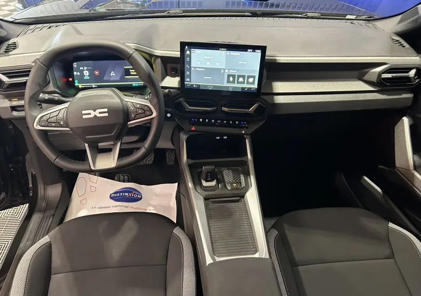 Vue intérieure avant du tableau de bord et volant du Dacia Bigster 2026, avec écran tactile central et finitions tissu noir.