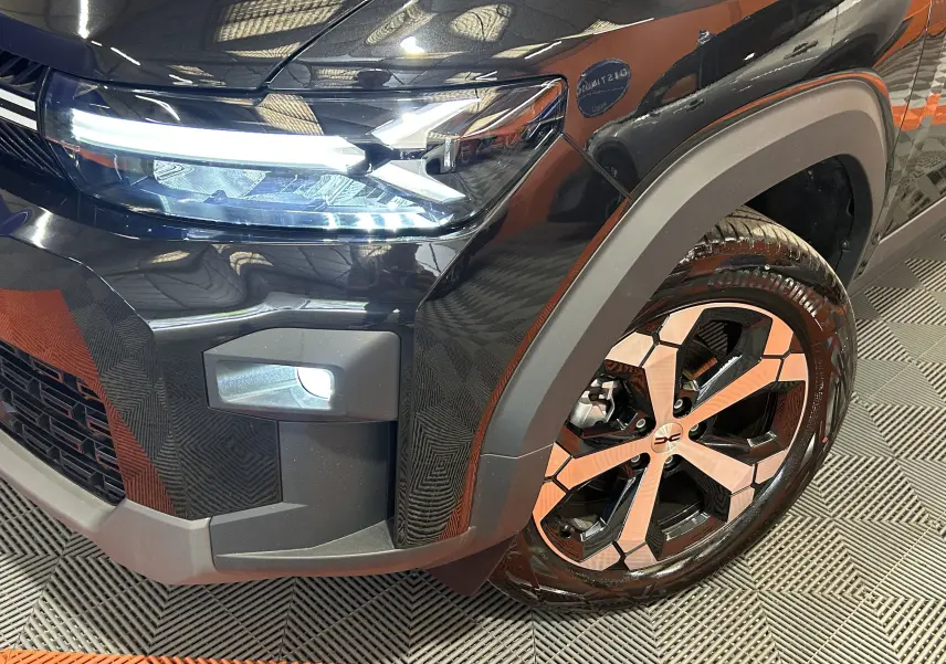 Gros plan sur l'avant droit noir nacré du Dacia Bigster 2026, mettant en valeur le phare LED et la jante alliage distinctive.