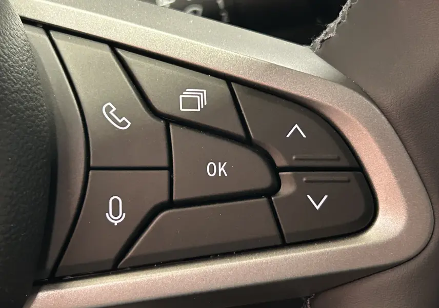 Gros plan sur les commandes multifonctions au volant du Dacia Bigster 2026, boutons noirs avec icônes blanches.