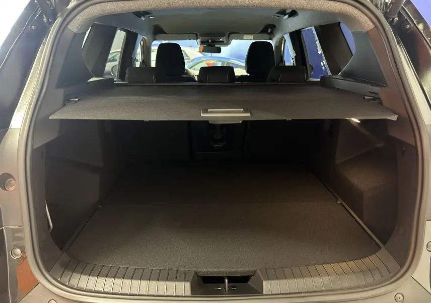 Coffre ouvert vu de l'arrière d'un Dacia Bigster noir nacré avec cache-bagages et sièges arrière visibles.