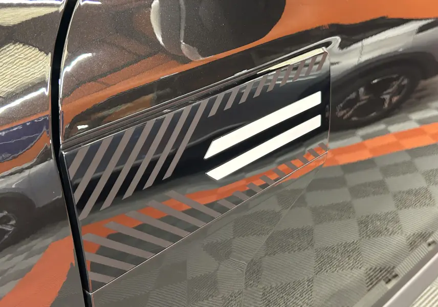 Détail du côté gauche noir nacré du Dacia Bigster 2026 avec motif graphique et surface brillante réfléchissante.