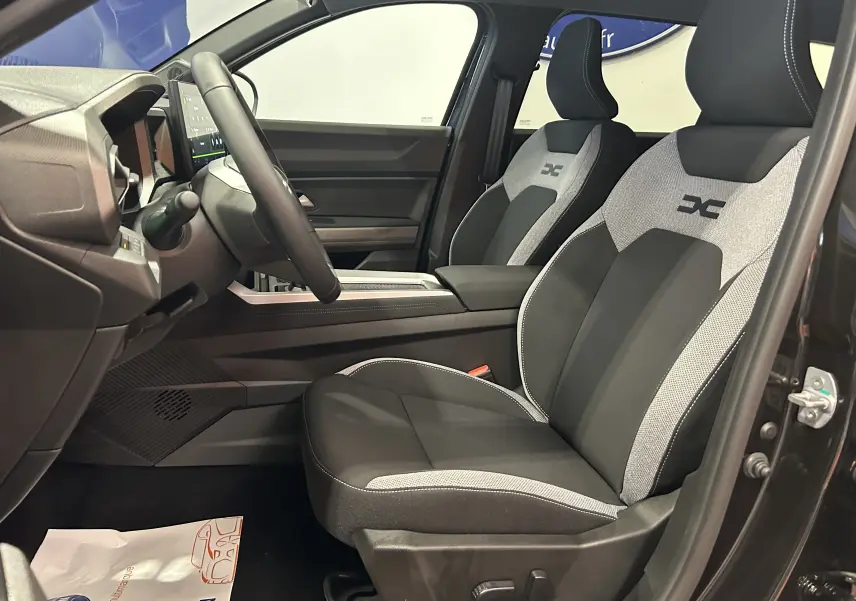 Vue intérieure côté conducteur du Dacia Bigster noir nacré, mettant en valeur les sièges tissu bi-ton avec logo distinctif brodé.