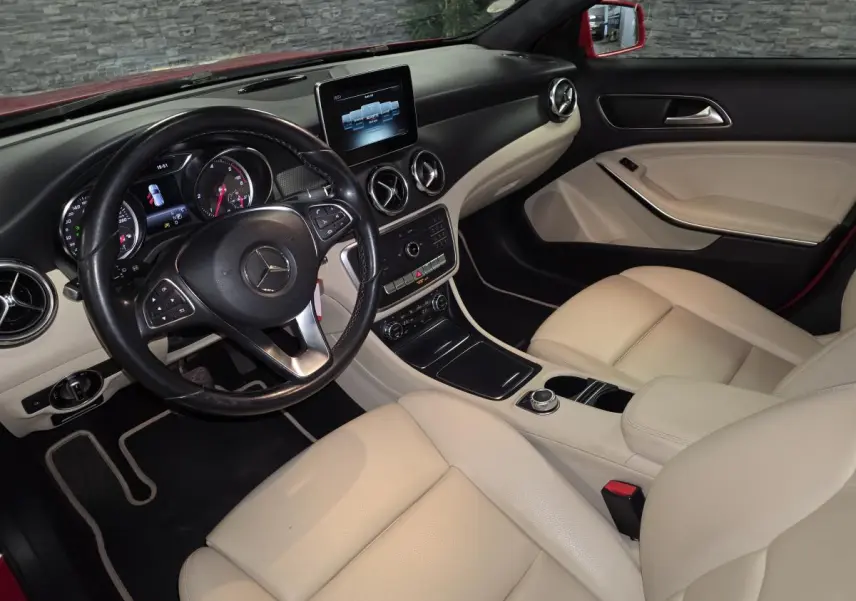 Vue intérieure côté conducteur d'une Mercedes GLA 200 d rouge, sièges en similicuir clair et tableau de bord noir.