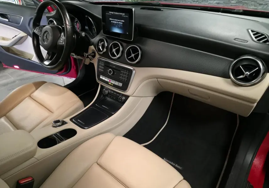 Vue intérieure côté conducteur d'une Mercedes GLA 200 d rouge, avec sièges beige et tableau de bord bicolore noir et beige.