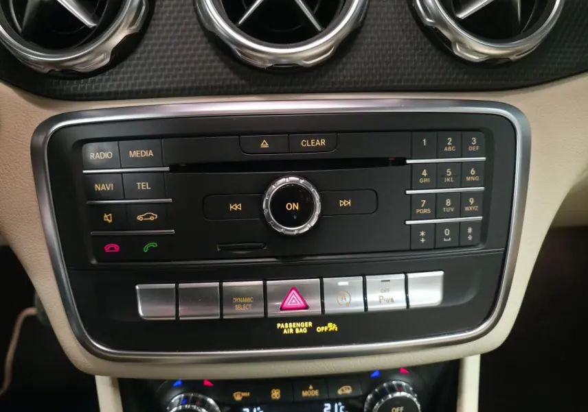 Vue rapprochée de la console centrale beige du Mercedes GLA 200 d rouge, avec commandes multimédia et climatisation.
