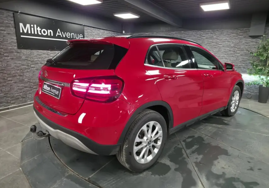 Vue 3/4 arrière droite d'un Mercedes GLA rouge avec attelage rabattable et jantes alliage 17 pouces en showroom.