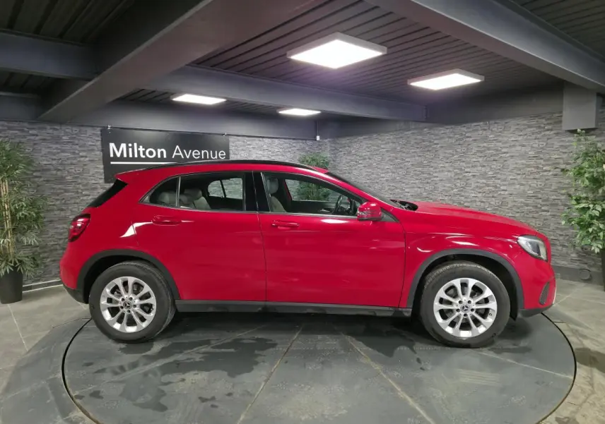 Vue de profil côté gauche d'un Mercedes GLA 200 d rouge avec jantes alliage 17 pouces dans un showroom.