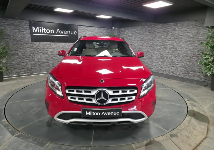 Vue avant d'un Mercedes GLA 200 d rouge brillant avec calandre chromée et logo étoile au centre, en showroom.