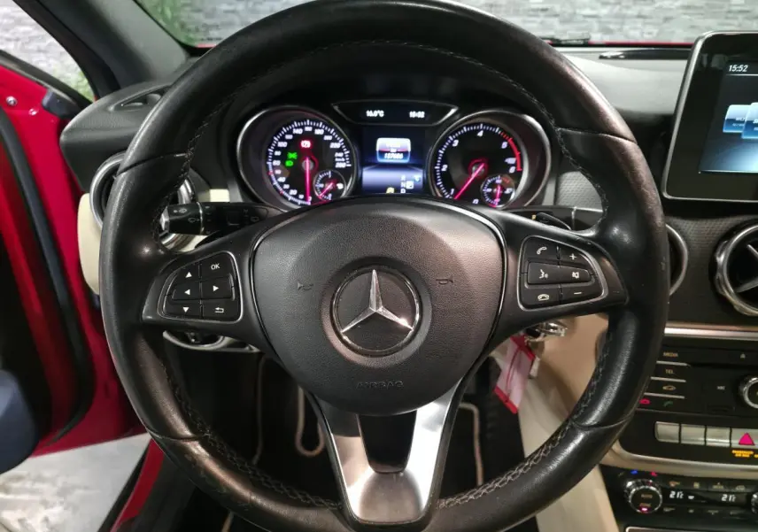 Vue centrée sur le volant cuir noir d'une Mercedes GLA rouge, avec tableau de bord et écran multimédia visibles.