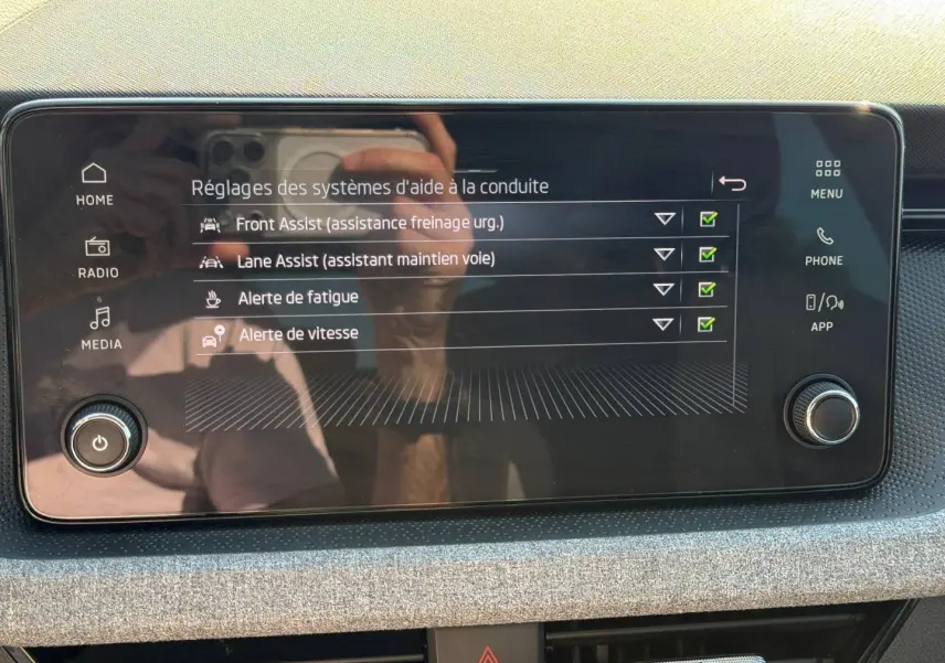 Écran tactile central du Skoda Scala 2025 montrant les réglages d’aide à la conduite, avec cadre noir et tableau de bord gris.