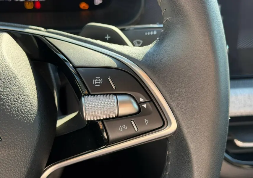 Gros plan sur les commandes gauche du volant cuir noir du Skoda Scala gris, avec molette et boutons multifonctions.