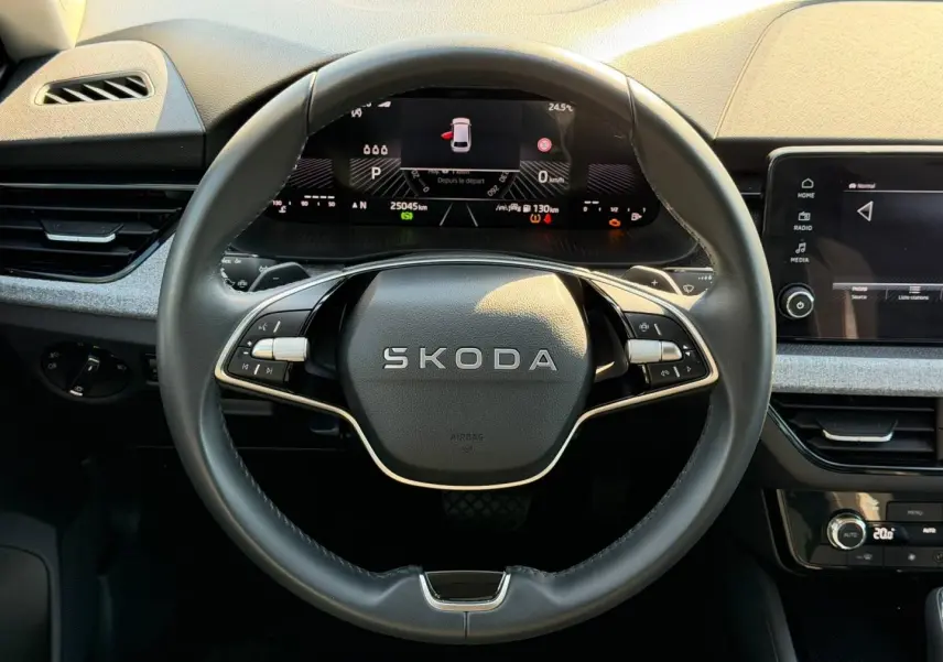 Vue intérieure centrée sur le volant cuir noir SKODA avec tableau de bord numérique et écran tactile gris clair.