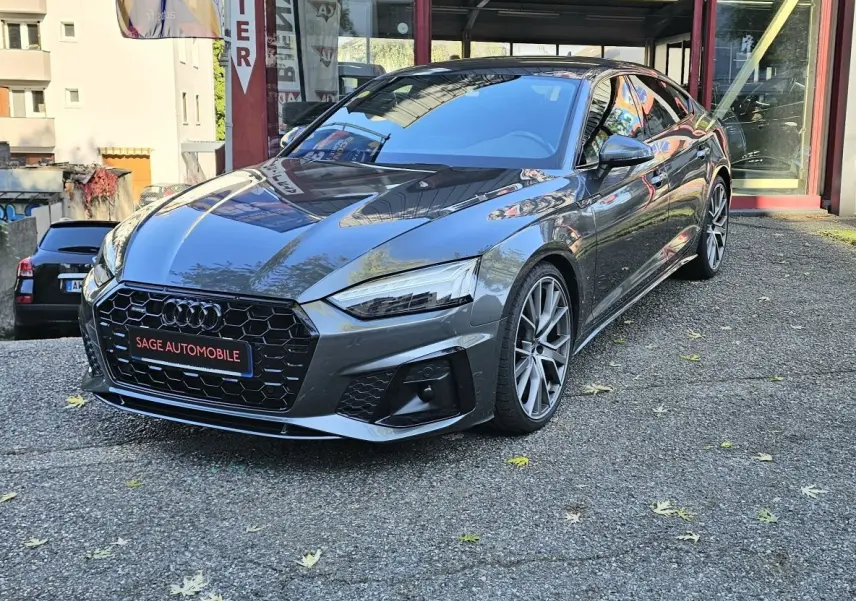 Audi A5 Sportback gris Daytona en 3/4 avant droit, avec calandre hexagonale noire et jantes alliage distinctives.