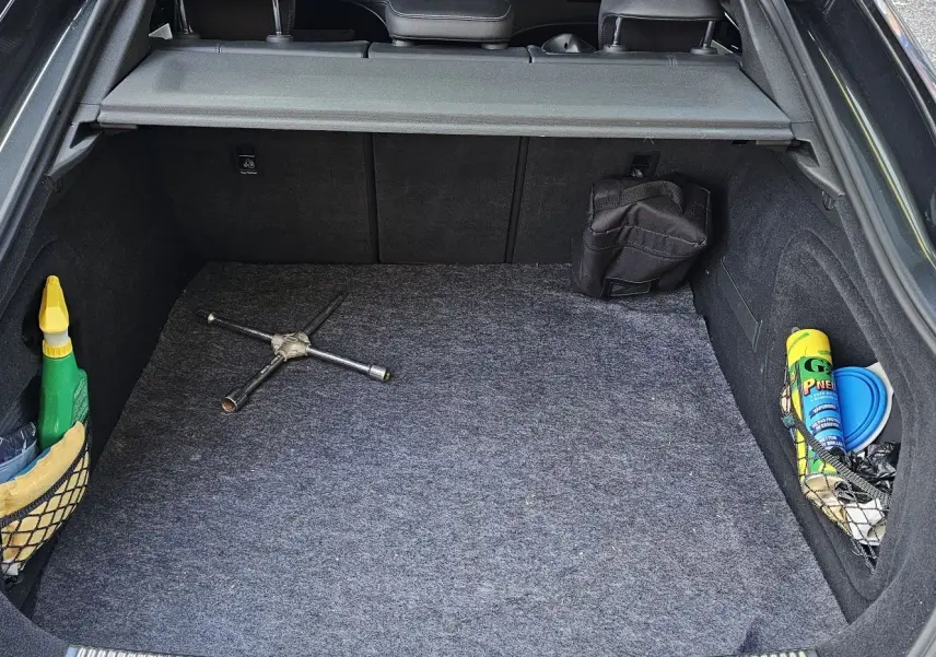 Coffre ouvert d'une Audi A5 Sportback gris Daytona, montrant un cric en croix et des accessoires de rangement latéraux.