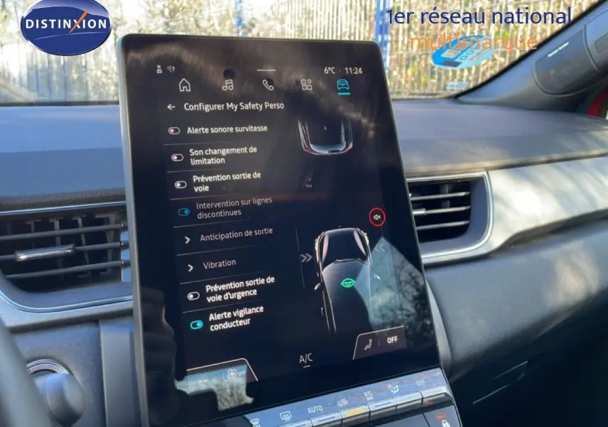 Vue rapprochée de l'écran tactile central du tableau de bord du Renault Captur rouge désir métal avec toit noir, affichant les aides à la conduite.