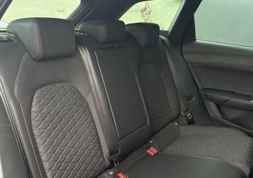 Vue latérale droite de la banquette arrière noire avec surpiqûres rouges et sellerie matelassée du SEAT Leon 2025.