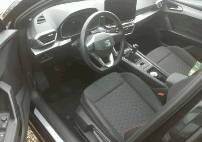 Vue intérieure côté conducteur du SEAT LEON ST 2025, volant multifonction cuir et sièges sport noirs avec surpiqûres rouges.