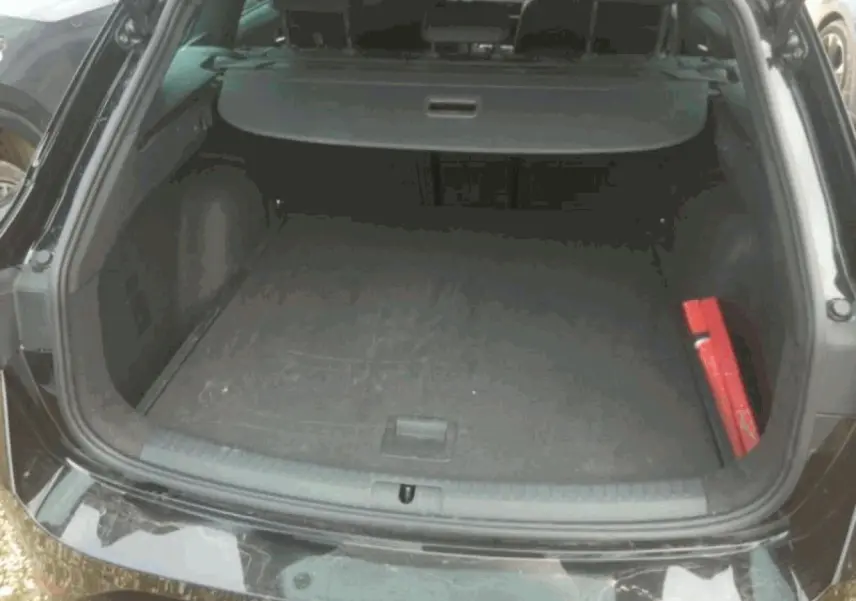 Coffre ouvert vu de l'arrière d'une SEAT LEON ST noir minuit, avec cache-bagages et kit de sécurité rouge visible.