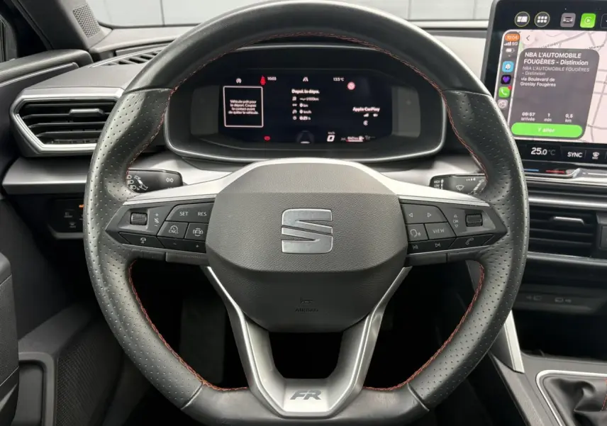 Vue rapprochée du volant en cuir noir avec surpiqûres rouges et tableau de bord numérique du SEAT Leon 1.5 e-TSI FR 2025.