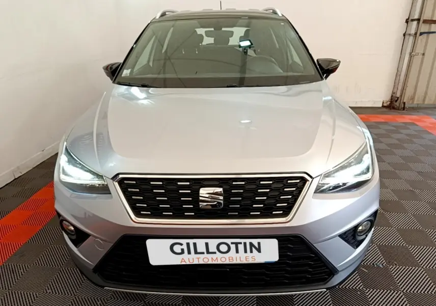Vue avant d'un SEAT Arona gris clair 2019 avec feux LED allumés dans un showroom.