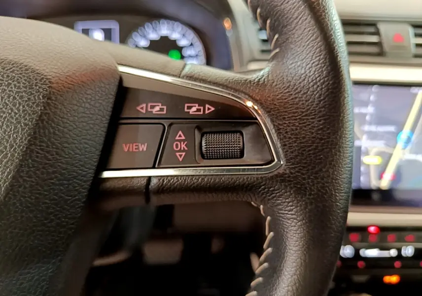 Gros plan sur le côté gauche du volant cuir et alu du SEAT Arona 2019 avec commandes multifonctions et écran tactile en arrière-plan.