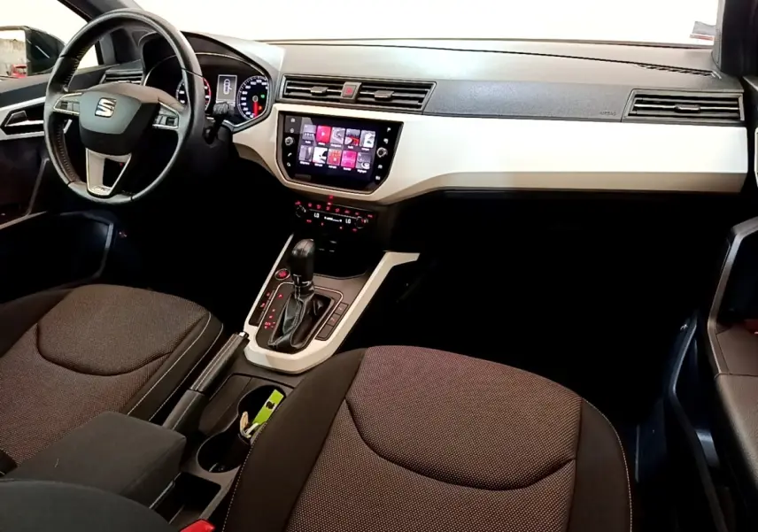 Vue intérieure avant droite du SEAT Arona gris clair 2019, volant cuir alu et écran tactile central visible.