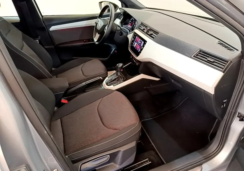 Vue intérieure côté conducteur du SEAT Arona gris clair, mettant en valeur le tableau de bord moderne et les sièges tissus noirs.