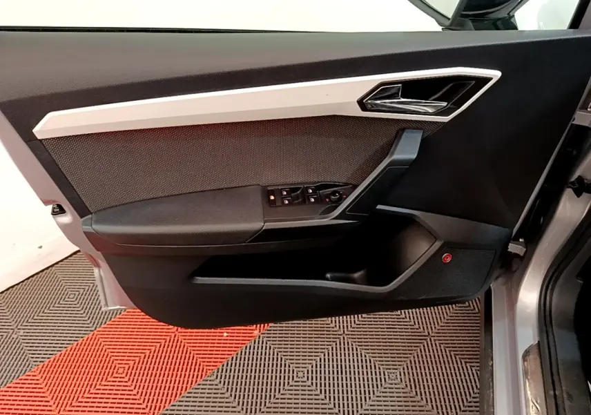 Vue latérale du panneau de porte avant gauche gris clair de la SEAT ARONA avec commandes de vitres et poignée chromée.