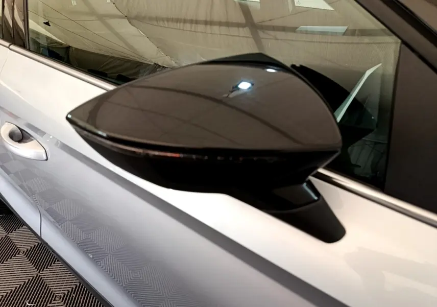 Rétroviseur noir en gros plan sur le côté gauche d’une SEAT Arona gris clair, avec poignée de porte visible.