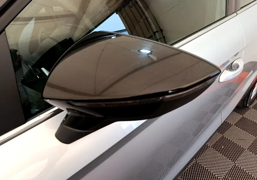 Gros plan sur le rétroviseur droit noir brillant d'une SEAT Arona gris clair, avec partie latérale et poignée de porte visibles.