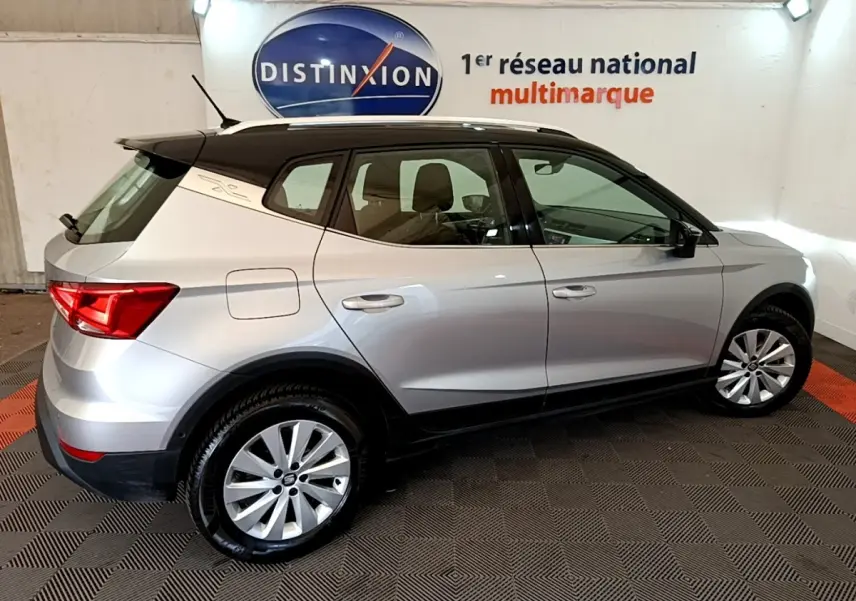 Vue de profil côté droit d'un SEAT Arona gris clair avec toit noir et jantes alliage dans un showroom.
