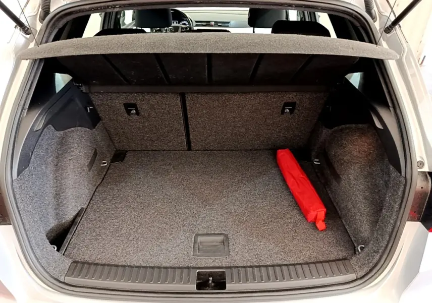 Coffre ouvert d’une SEAT Arona gris clair, vue arrière, avec tapis gris et un objet rouge posé à droite.