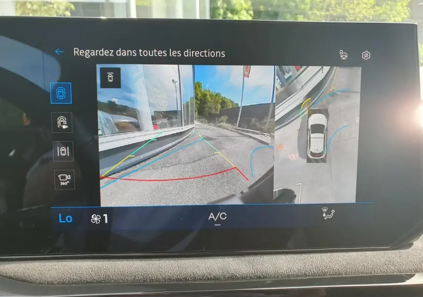 Écran intérieur montrant l’aide au parking 360° de la Renault Clio VI gris Rafale avec vue arrière et vue aérienne du véhicule.