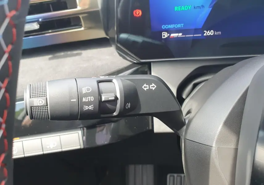 Gros plan sur la commande des feux et clignotants à gauche du volant dans le tableau de bord gris de la Renault Clio VI hybride.