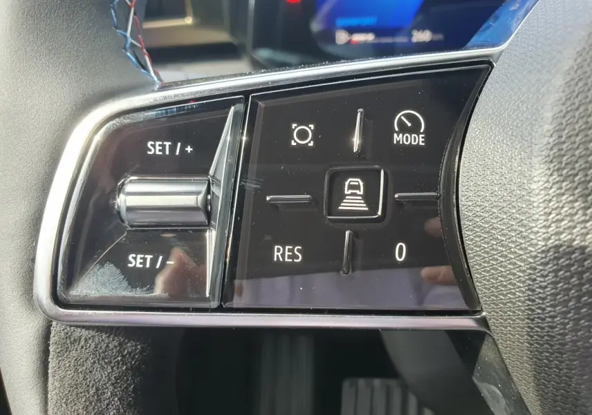 Gros plan sur les commandes au volant côté gauche de la Renault Clio VI hybride, finition Esprit Alpine, avec boutons de régulateur et mode conduite.