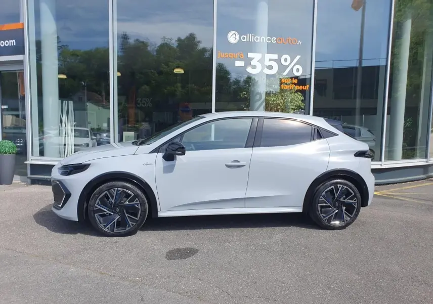 Profil droit de la Renault Clio VI gris Rafale 2026 avec jantes alliage 18” et vitres teintées, devant une vitrine.