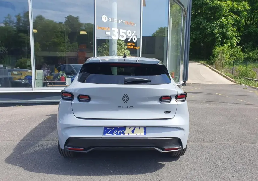 Vue arrière d'une Renault Clio VI gris Rafale avec feux LED et logo distinctif, stationnée devant un bâtiment vitré.